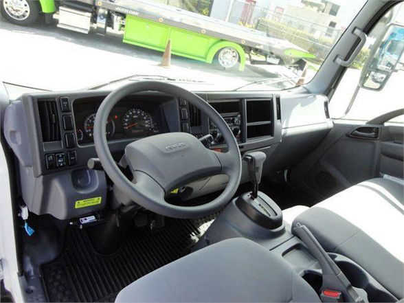Interior of a 2024 Isuzu NPR HD dump truck cab showing steering wheel, dashboard, gear shifter, and driver seat.