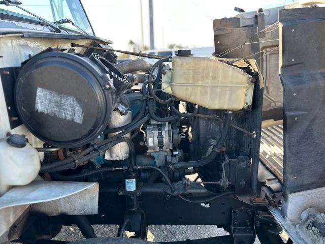 Truck engine bay showing air filter canister, coolant reservoir, hoses, and radiator support on a 1997 International 4700 box truck.