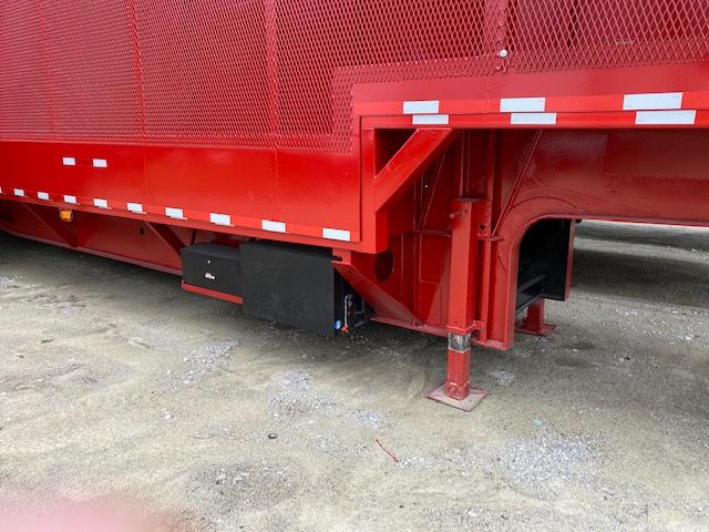 Crush car carrier trailer lower corner with red sides, black toolbox, and support legs visible.