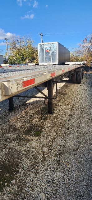 Flatbed trailer with utility combo features, side view showing metal frame, support legs, and gooseneck hitch area.