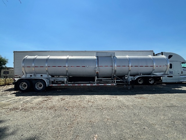 2011 Heil 407 crude oil tanker trailer (tanker) attached to truck, side view showing cylindrical stainless steel tank with red reflective stripe and multiple axles.