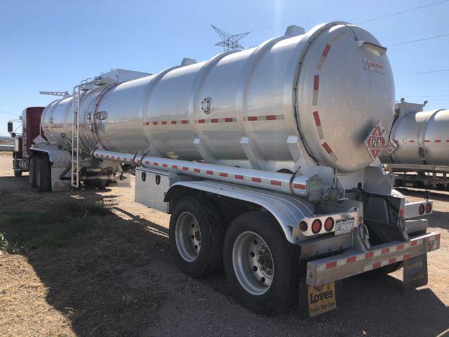 A white cylindrical tanker trailer labeled with hazmat placard on the rear, mounted on a dual-axle trailer, with a ladder and rear bumper visible.
