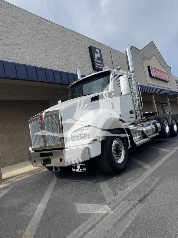 Kenworth T880 conventional daycab truck in a dealership lot, white with chrome grille and exhaust stacks, front-left angle view.