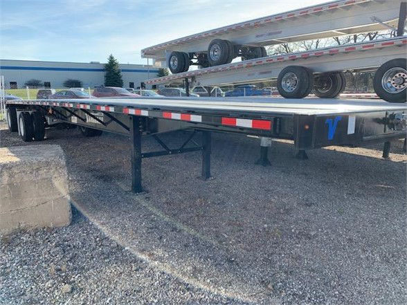 Flatbed trailer with stacked steel deck sections and black legs, 48ft Vanguard trailer in an outdoor lot.