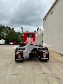 Rear view of a red Kenworth truck tractor with black bumper fenders, showing dual rear wheels, mud flaps, and license-plate area; no visible text on vehicle; cloudy sky.