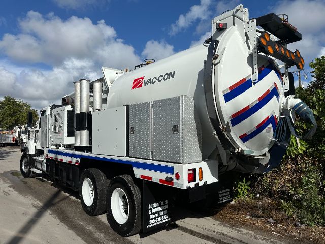 Vacuum truck by Vaccon with large cylindrical tank, rear outlet, chrome exhausts, and blue/red stripes. Freightliner 114SD chassis visible.