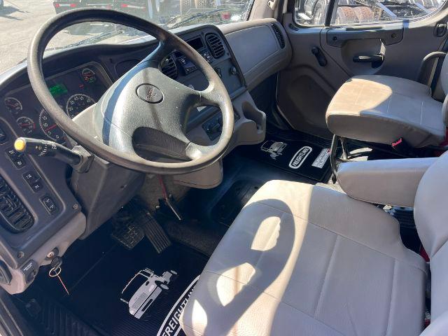 Cab interior of a 2018 Freightliner M2 106 dump truck showing steering wheel, driver's seat, and dashboard with pedals.