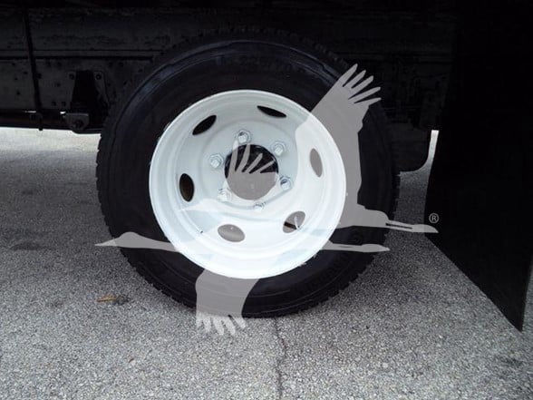 Isuzu NPR HD wheel and tire on a truck, white steel wheel with five holes and lug nuts, part of a box truck chassis.