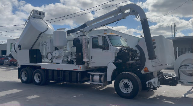 Vacuum truck on a flatbed with large rear tank, hose reel arm and engine bay exposed; Sterling L8500 chassis in serviceable condition.