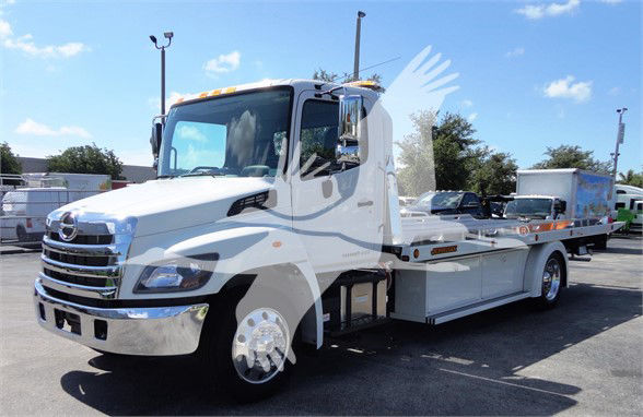 Tow truck with white cab and flatbed, chrome grille, showing Hino emblem; appears to be a 2022 Hino 268A tow truck. Text on image not clearly legible other than brand features.