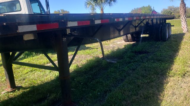 Flatbed trailer undercarriage showing support legs and frame with reflective tape along the side.