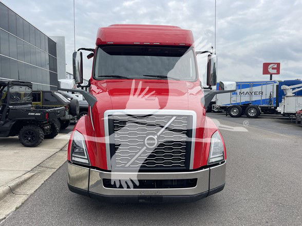 Front view of a red 2022 Volvo VNL64T740 truck. Visible grille with Volvo emblem, large front bumper, and side mirrors. Foreground shows windshield with tinted glass and headlights.