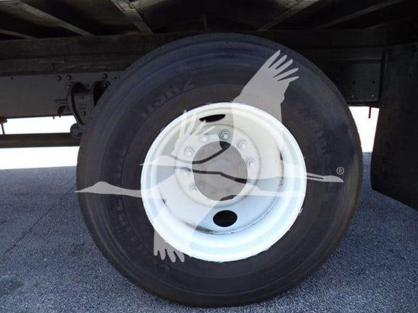 Truck wheel and rim under trailer showing tire with white steel wheel and hub, no visible text legible on tire.
