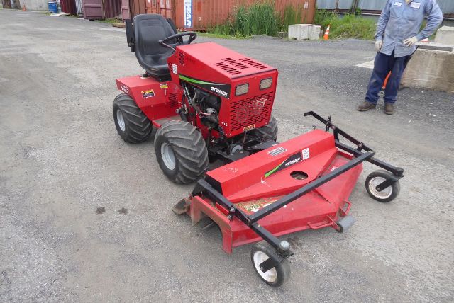 Red Steiner 415 compact tractor with a mower attachment in an outdoor lot, two men in the background.