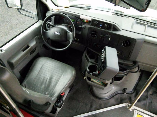 Ford E-450 bus interior showing driver seat, steering wheel with Ford emblem, dashboard, and center console with various controls.