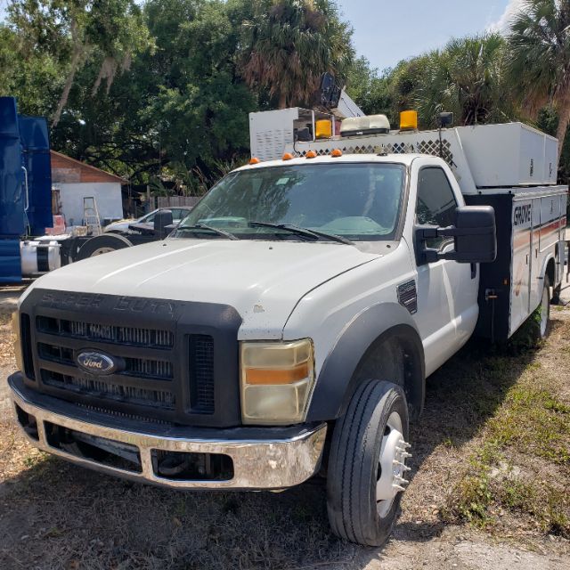 Ford Super Duty tow service utility truck with utility bed and equipment on top. Front grille shows Ford logo; front bumper chrome; amber cab lights on roof; side mirrors extended.