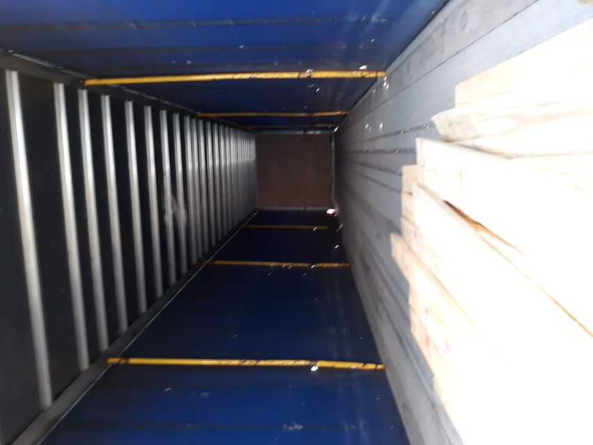 Interior of a blue utility trailer with wooden boards on the floor, yellow supports along the walls, and a distant rear doorway.