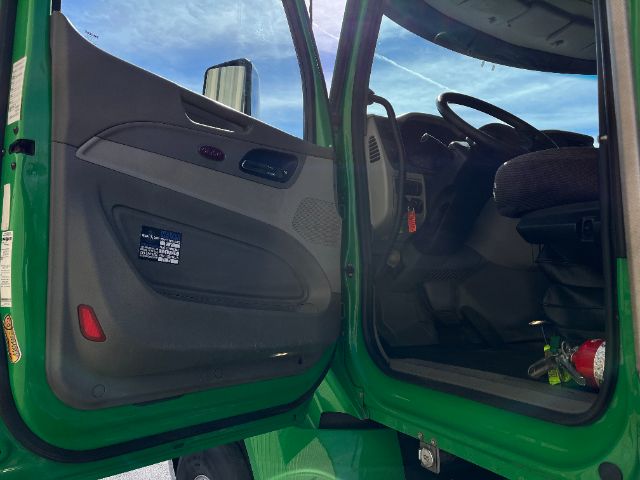 Truck interior with open driver door showing gray door panel, steering wheel, dashboard, and green exterior.