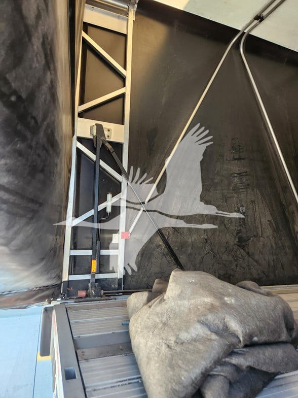 Trailer interior with curtainside cargo area and ladder, branding eagle silhouette on black wall, tarp and metal framing visible.
