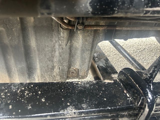 Truck undercarriage view showing metal frame, bolts, and dirt; no legible labels or fluid reservoirs visible.