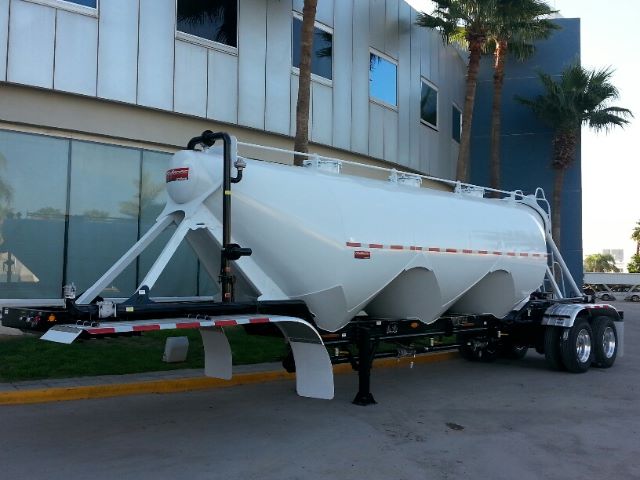 Trailer with a large white pneumatic dry bulk tank on a dual-axle trailer, showing geometric support frames at the front and a long cylindrical tank with side access ladders and reflective striping.