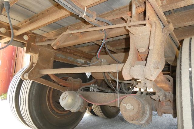 Underneath trailer chassis with leaf spring suspension, axles, and wheels; rusted metal components and wiring visible.