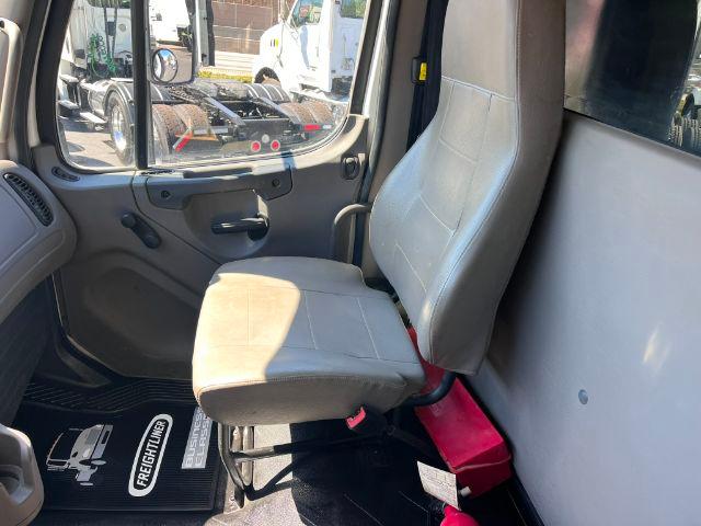 Freightliner M2-106 truck cab interior showing gray driver seat and door panel with window, door handle, and floor mat.