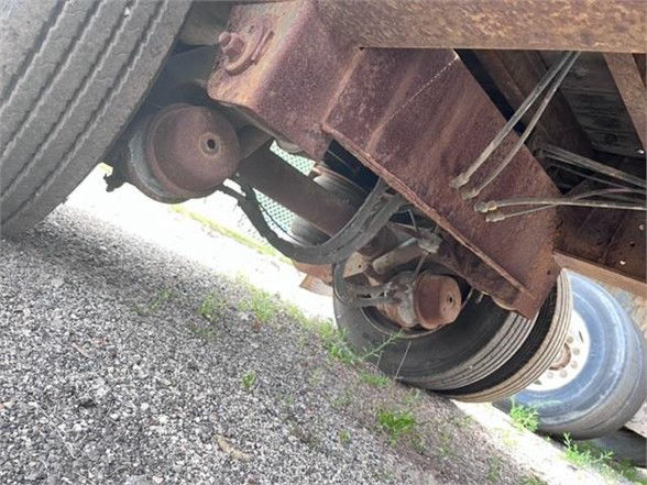 Trailer undercarriage showing wheel axles, drum brakes, leaf springs, and rusted frame of a Fontaine ELITE drop deck trailer.