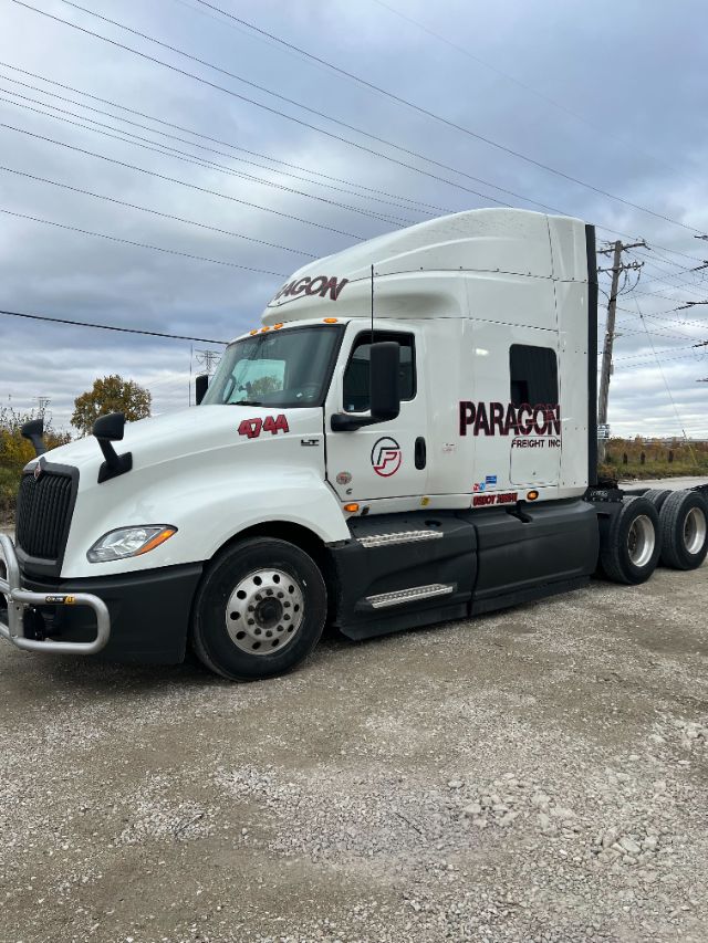 Truck side view showing 2019 International LT625 conventional sleeper with Paragon Freight Inc branding, white cab, 4x4 badging, dual rear axles, and chrome steps.