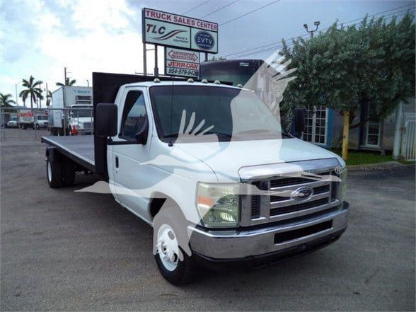 Flatbed truck showing Ford E-Series van with flatbed in a dealership lot.