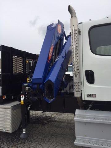 Truck with knuckle boom crane mounted on cab; blue crane arm with orange logo; white cab with window; vertical ladder-like support; some equipment mounted behind cab.
