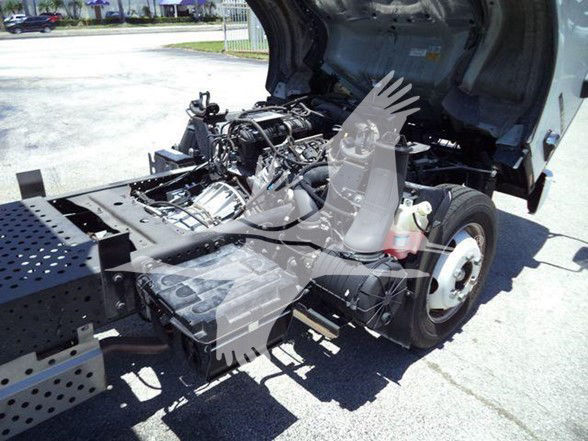 Isuzu NQR truck chassis with engine bay visible, rear cab area open, showing fluid reservoir and wiring harness.