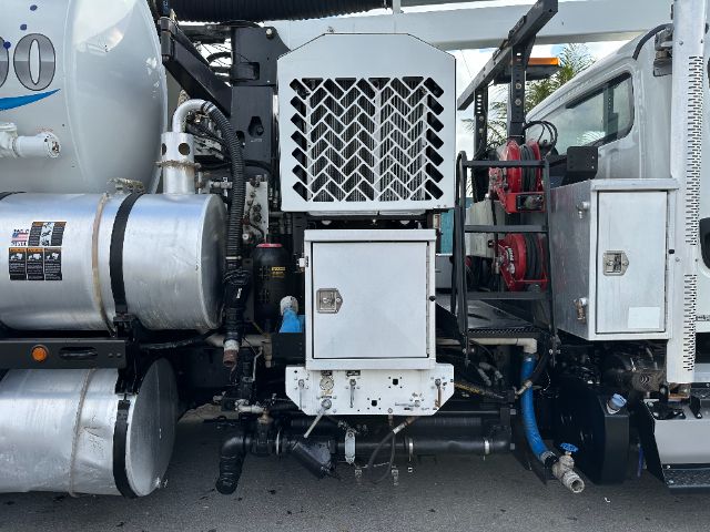 Freightliner M2 engine bay side showing cooling fan guard, cylindrical tanks, hoses, and a front service access panel with metal grille.
