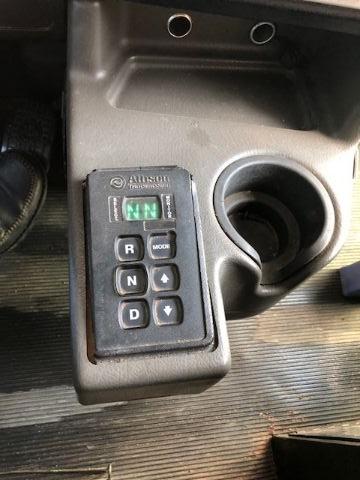 Cockpit area showing digital gear selector with PRNDS and a small green indicator display, plus a cup holder.