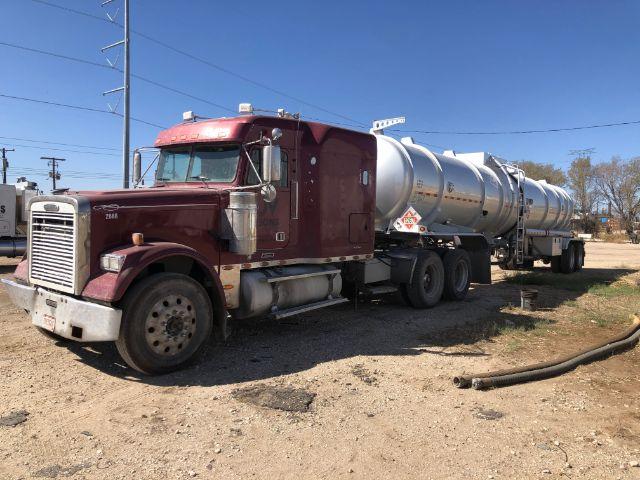 2007 Freightliner Classic Conventional chassis with maroon truck cab and attached silver tanker trailer, parked on dirt lot.