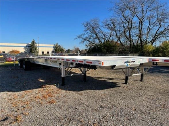 Flatbed trailer showing aluminum Fontaine Revolution long deck with dual axles and support jacks.