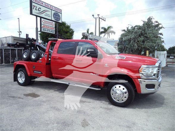 Tow truck: red 2024 Ram 5500 Laramie with dual rear wheels, flatbed equipment, and a spare tire mounted on the bed. visible text includes RAM 5500 badge and dealership signage in background.