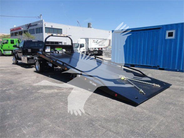 Flatbed tow truck with long black steel bed and ramp in front, Ram 5500 SLT badge not visible, background shows a dealership lot.