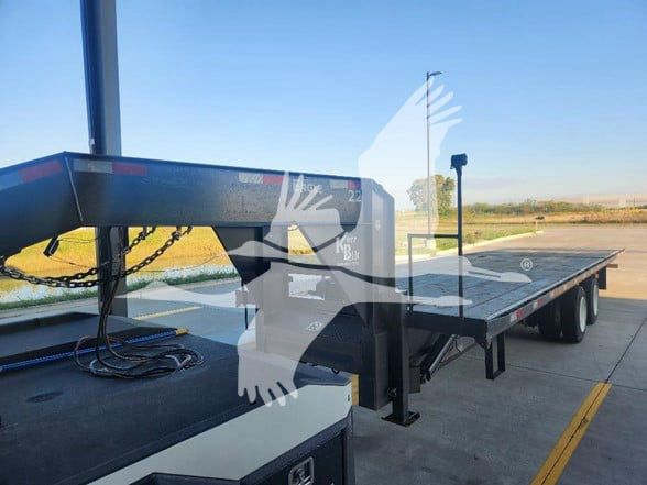 Flatbed trailer showing landing gear and long platform with black frame; chain and equipment visible near the hitch area.