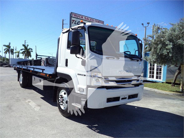 Isuzu flatbed tow truck in white, front-left view, with a long flat bed. Visible are the cab with large windshield, side mirrors, and Isuzu badge on grille.