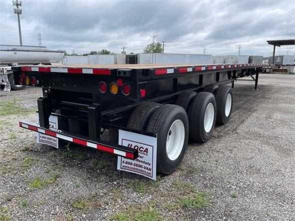 Fontaine XCALIBUR extendable flatbed trailer with dual rear triple-axle setup, black frame, white wheels, red/white reflective tape along edges, stock numbers and signage on rear corner.