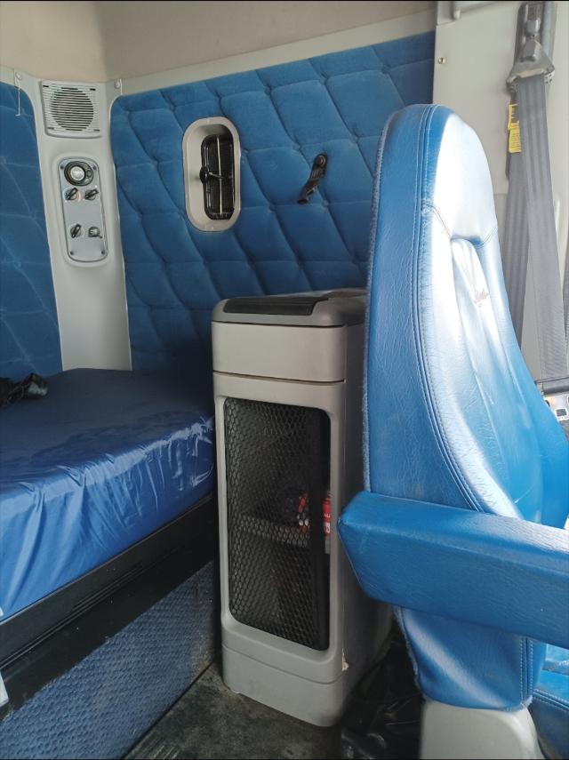 Freightliner Columbia cab interior showing blue quilted sleeper area, seating, and a small cabinet with a mesh door.