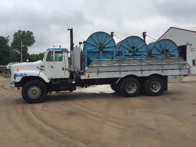 View of a white 1991 International 2674 service truck with a flatbed carrying three large blue spool reels.