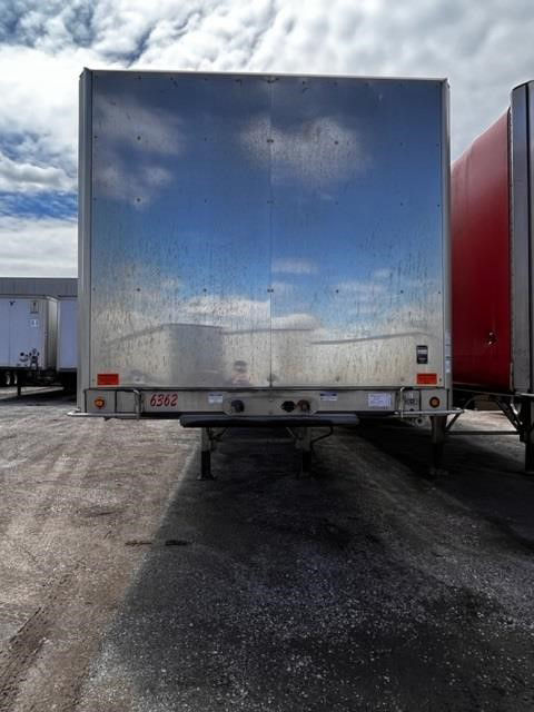 Flatbed trailer rear view with rolling tarp, metal sides, undercarriage and light assembly visible.