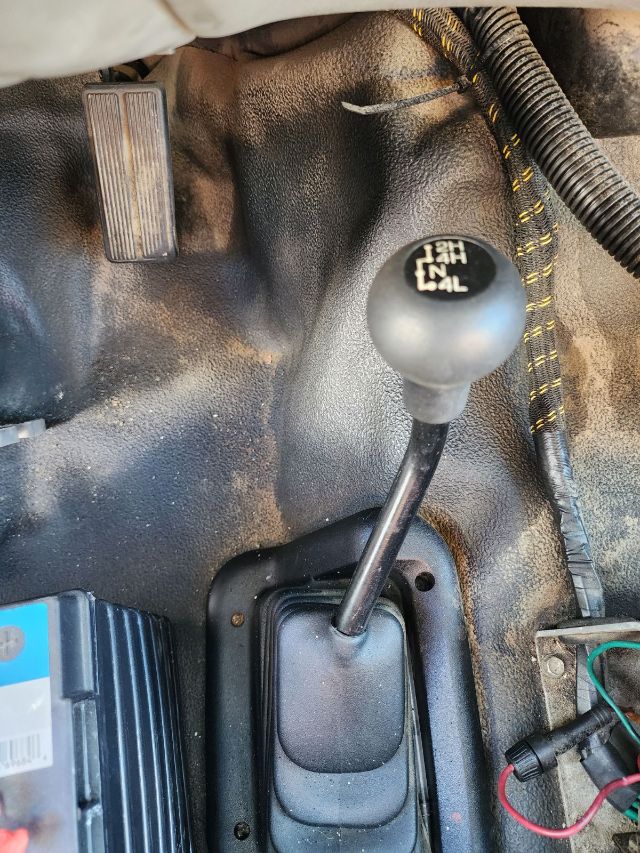 Manual shift lever in center console of a Ford F-550 with surrounding pedals and wiring visible.