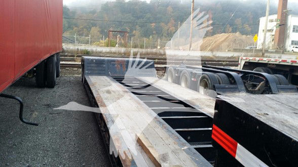 Trailer in a yard showing Kalyn Siebert mechanical removable lowboy trailer with steel deck and cutouts, viewed from side near cab and rails.