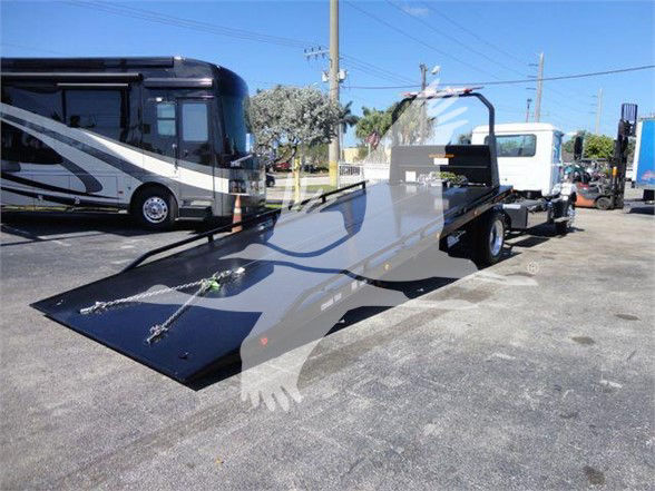 MD6 tow truck with a flatbed bed in foreground, utility truck in background, pickup and dealership lot.