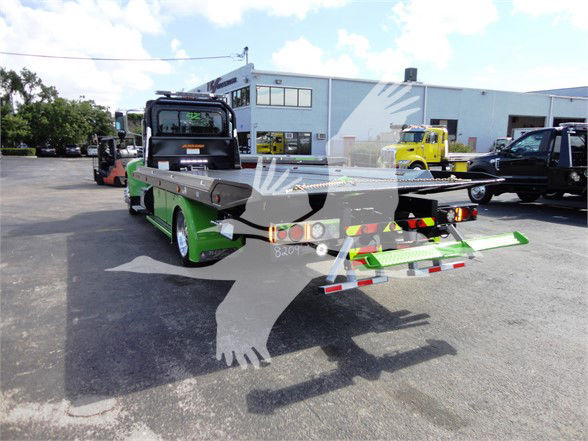 Peterbilt 337 tow truck with green-and-black two-vehicle carrier bed at a dealership lot.