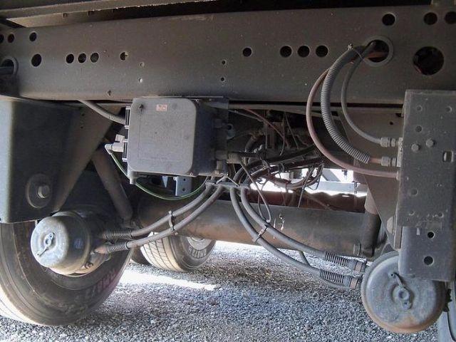 Trailer underside showing electrical box and wiring harnesses, frame rails, brake lines, and leaf spring suspension.