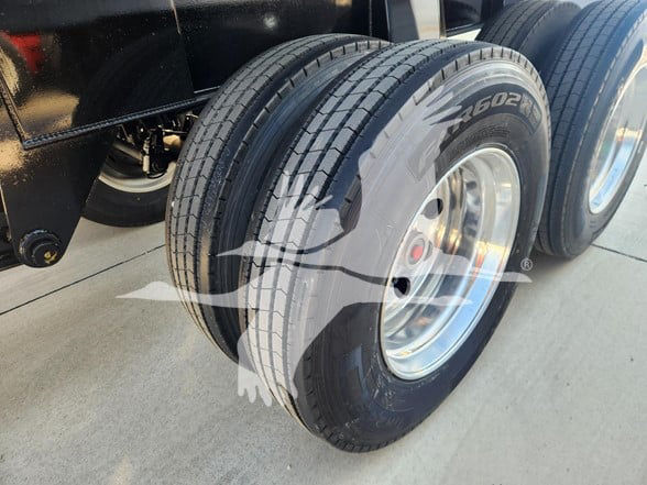Dual rear axles with dual tires on a dump trailer. Visible tread, rims silver, and part of the undercarriage. No legible brand or model text.